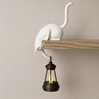 Cat shelf hanger on a wooden shelf holding a lit lantern