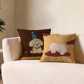 Winnie Party Poodle Cushion, brown cushion with a cream poodle in a blue party hat, shown beside the mustard puppy cushion