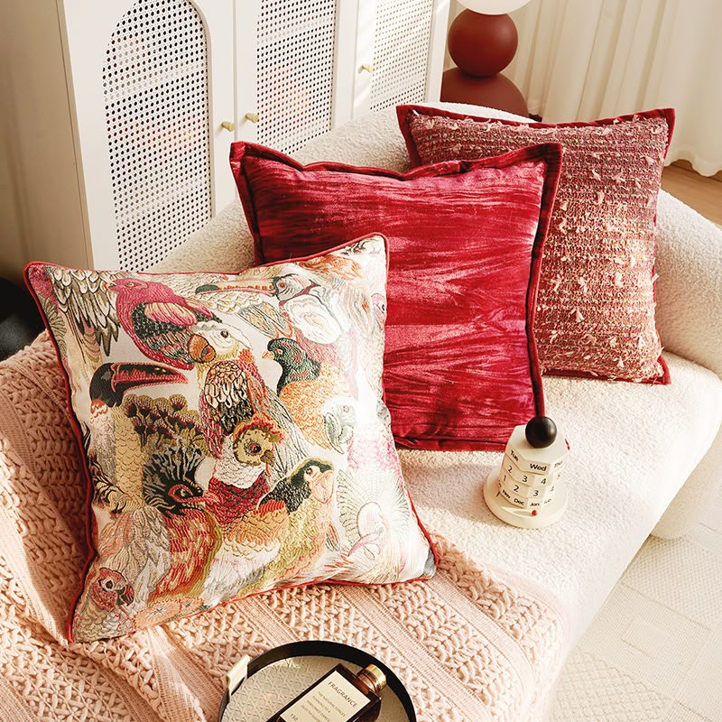 Cressida Bird Tapestry Cushion with the matching red cushions on a daybed