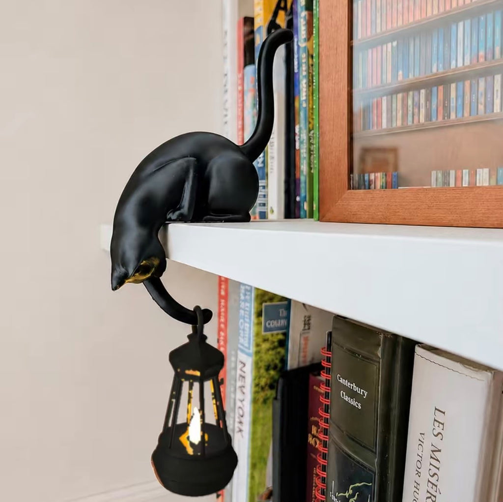 Cat shelf hanger draped over a bookshelf edge with a glowing lantern
