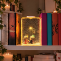 Clara first snow book lamp glowing on a bookshelf between hardback novels